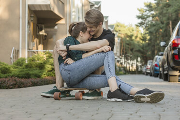 Glückliches junges Paar, das sich umarmt, während es auf einem Skateboard im Freien sitzt - FSIF01399