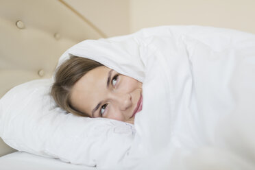 Nachdenkliche Frau, zugedeckt mit Bettdecke, die wegschaut, während sie sich zu Hause im Bett entspannt - FSIF01401