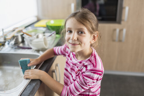 Portrait of smiling girl holding cleaning sponge at kitchen sink - FSIF01407
