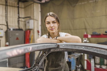 Porträt einer selbstbewussten Mechanikerin, die sich in einer Werkstatt an ein Auto lehnt - FSIF01410