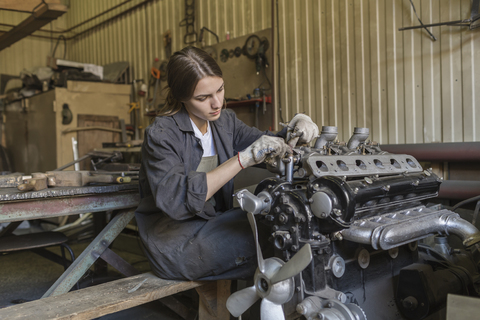 Mechanikerin repariert Automotor in einer Werkstatt, lizenzfreies Stockfoto