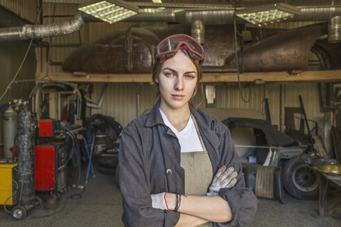 Porträt einer selbstbewussten Mechanikerin mit verschränkten Armen in einer Werkstatt - FSIF01414