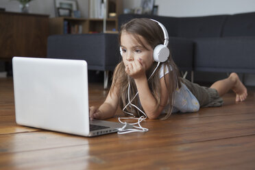 Mädchen, das einen Laptop benutzt, während es auf einem Hartholzboden Musik hört - FSIF01418