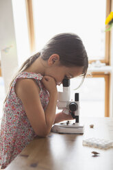 Seitenansicht eines neugierigen Mädchens, das in ein Mikroskop auf einem Tisch zu Hause schaut - FSIF01419