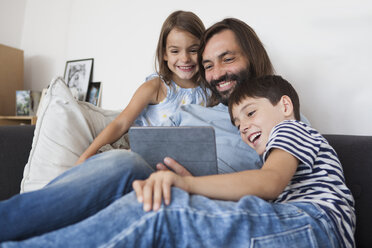 Glücklicher Vater mit Kindern, der auf dem Sofa zu Hause ein digitales Tablet benutzt - FSIF01420