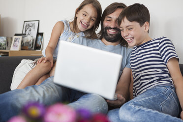 Cheerful father with children using laptop on sofa at home - FSIF01422