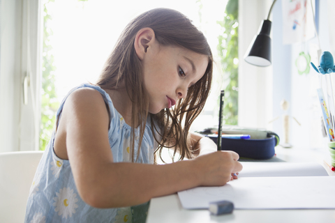 Seitenansicht eines Mädchens, das in einem Buch auf einem Tisch zu Hause schreibt, lizenzfreies Stockfoto