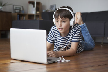 Junge hört Musik über Kopfhörer, während er einen Laptop zu Hause benutzt - FSIF01430
