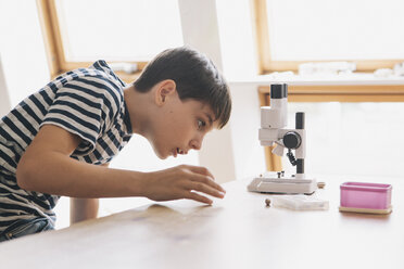 Neugieriger Junge betrachtet das Mikroskop auf dem Tisch im Haus - FSIF01431