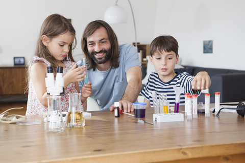 Vater und Kinder machen ein wissenschaftliches Experiment am Tisch im Haus, lizenzfreies Stockfoto