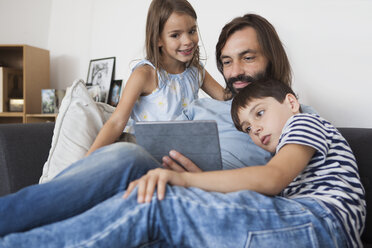 Vater mit Kindern nutzt digitales Tablet auf dem Sofa zu Hause - FSIF01436