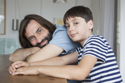 Porträt von Vater und Sohn am Tisch sitzend in einem Haus, lizenzfreies Stockfoto