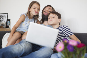 Father with children puckering in front of laptop while sitting on sofa - FSIF01438