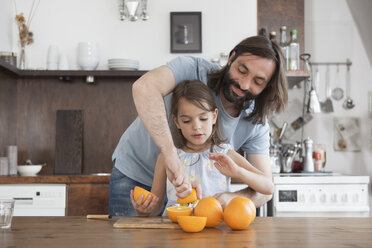 Vater hilft Tochter beim Auspressen von Orangen in der Küche - FSIF01440