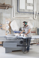 Full length of male carpenter using a sliding table saw in workshop - FSIF01444