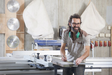 Portrait of happy male carpenter measuring lumber in workshop - FSIF01447