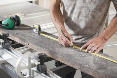 Midsection of male carpenter measuring plank on sliding table saw in workshop - FSIF01448