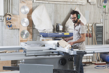 Male carpenter using a sliding table saw in workshop - FSIF01453