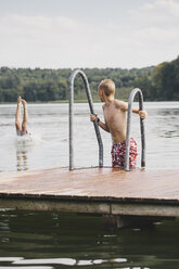 Boy looking at friend sticking out legs out of lake - FSIF01458