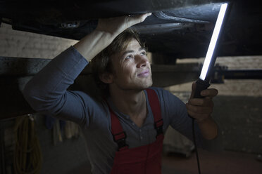 Mechaniker hält leuchtende Leuchtstoffröhre bei der Untersuchung eines Autos - FSIF01466