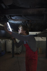 Mechaniker hält eine Leuchtstoffröhre in der Hand, während er die Unterseite des Autos untersucht - FSIF01468