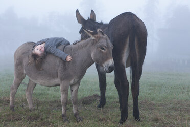Porträt eines Mädchens, das auf einem Esel auf einem Feld bei nebligem Wetter liegt - FSIF01478