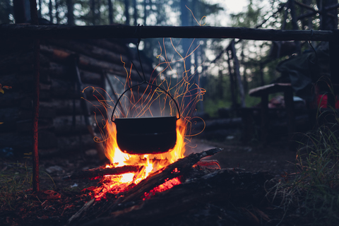 Container hanging over campfire in forest stock photo