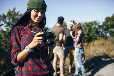 Junge Frau, die sich mit Freunden im Wald stehend Fotos auf der Kamera ansieht - FSIF01510