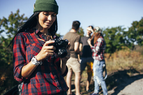 Young woman looking at photographs on camera with friends standing in forest - FSIF01510