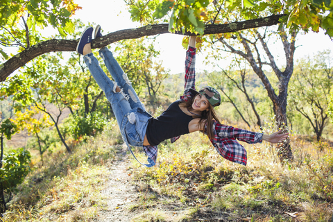 Full length of happy young woman climbing from branch in forest stock photo