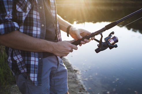 Midsection of man fishing at lakeshore in forest - FSIF01521