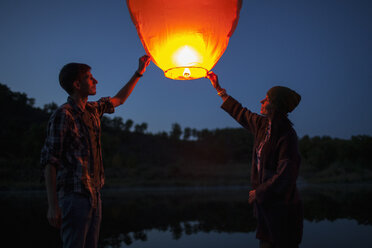 Man and woman releasing paper lanterns at lakeshore - FSIF01529