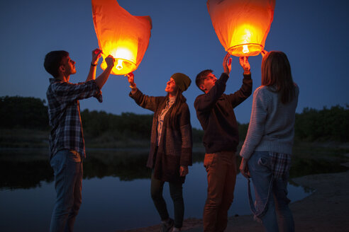 Male and female hikers releasing paper lanterns at lakeshore - FSIF01530