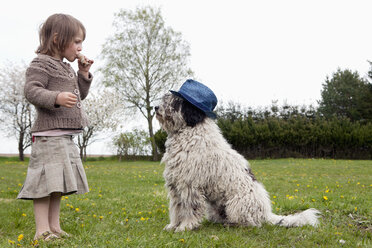 Full length side view of girl eating in front of dog on field - FSIF01533