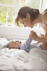 Side view of happy woman playing with baby boy lying on bed at home - FSIF01551