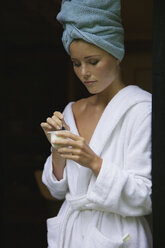 Young woman in bathrobe holding yoghurt in bowl at home - FSIF01552