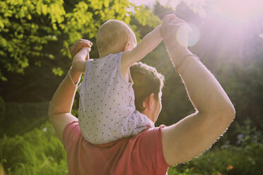 Rückansicht eines Vaters, der einen kleinen Jungen auf den Schultern trägt, auf einem Hof im Sommer - FSIF01564