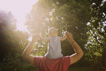 Rückansicht eines Vaters, der einen kleinen Jungen auf den Schultern trägt, im Hof an einem sonnigen Tag - FSIF01568