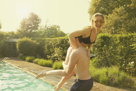 Man throwing cheerful woman in swimming pool during sunny day stock photo