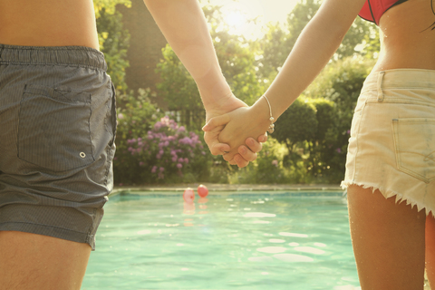 Rear view midsection of young man and woman holding hands while standing by swimming pool stock photo