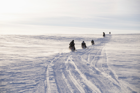 People driving snowmobiles on field against sky during winter stock photo