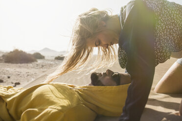 Romantic young woman looking at man lying on sand - FSIF01590