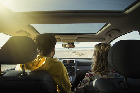 Rückansicht eines Paares im Auto am Strand an einem sonnigen Tag, lizenzfreies Stockfoto