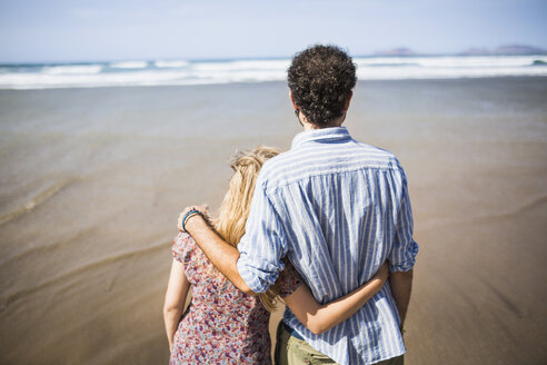 Rückansicht eines verliebten Paares, das sich am Strand in den Armen liegt - FSIF01597