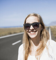 Lächelnde junge Frau mit Sonnenbrille auf der Straße - FSIF01602