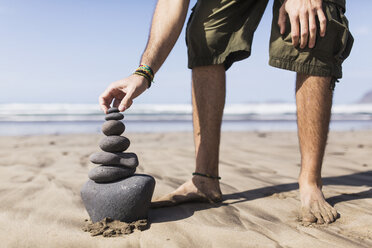 Niedriger Ausschnitt eines Mannes, der einen Stapel Steine am Strand balanciert - FSIF01603