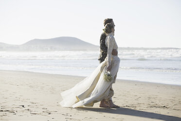 Full length side view of bride and groom standing arm around at beach - FSIF01628