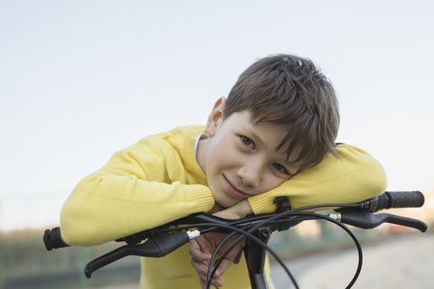 Porträt eines lächelnden Jungen, der sich gegen den klaren Himmel auf ein Fahrrad stützt, lizenzfreies Stockfoto