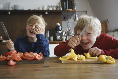 Happy brothers holding knives at table with vegetables in kitchen stock photo