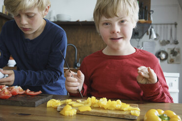 Porträt eines behinderten Jungen, der mit seinem Bruder am Tisch mit Gemüse in der Küche sitzt - FSIF01650